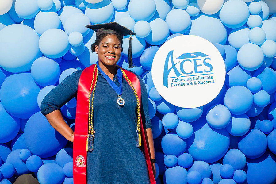 ACES graduate posing for a picture in front of blue balloon decorations